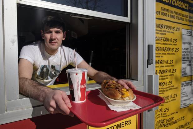 Manager Keaton Pridham serves a hot dog at the take-out window of Calgary's Tubby Dog on Feb. 23, 2018.