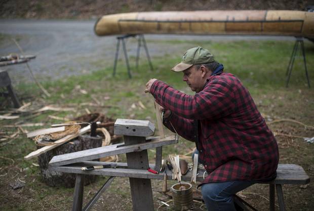 Todd Labrador straddles the draw horse while shaving wooden pegs to hold the canoe's gunwale cap in place.