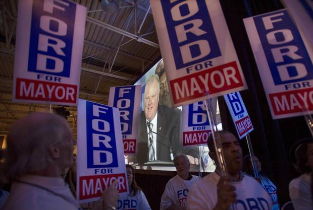 Rob Ford supporters hold signs as Ford is seen on a video screen during his 2014 campaign kick off.