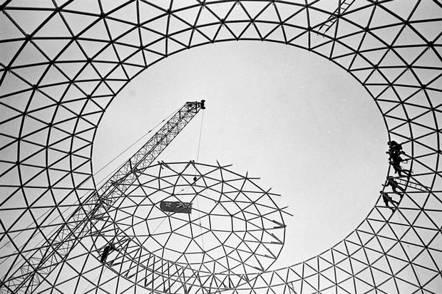 Workmen wait on dome for crane to finish maneouvring the cap of Cinesphere into position, Oct. 26, 1970.