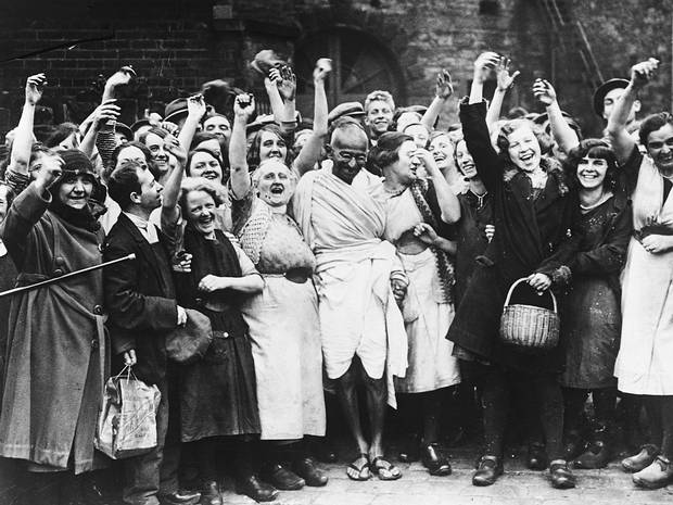 Gandhi acknowledges the cheers of young women workers outside Greenfield Mill in Darwen, Lancashire as part of his study of labour conditions in the English cotton industry. UK, 1931.