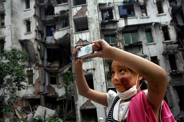 Nine-year-old Xia Xueyin, her face badly bruised from a fall an earthquake, takes photos of her family's damaged home in Hanwang town on May 22, 2008.