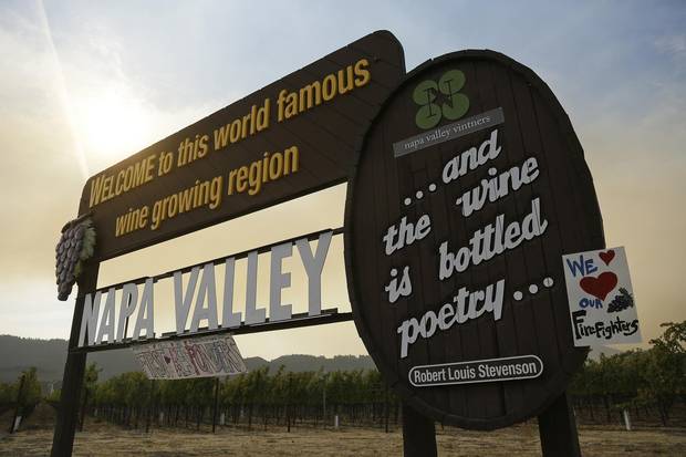 Smoke from the Nuns fire wafts over the Welcome to the Napa Valley sign on Oct. 16 in Oakville, Calif.