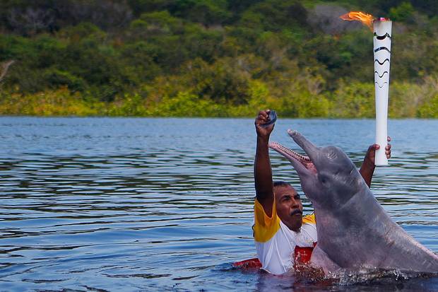Resident Davi Souza gives a fish to a pink river dolphin as he takes part in the Olympic flame torch relay at Solimoes River in Iranduba city, Brazil, on Monday.