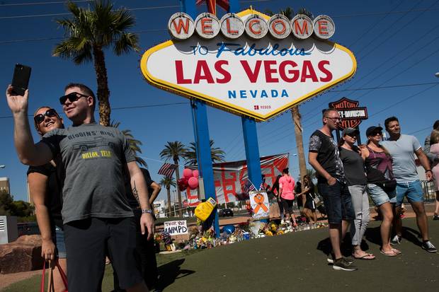 With a small makeshift memorial for Sunday's mass shooting victims below the 'Welcome to Fabulous Las Vegas' sign, visitors pose for photos by the iconic sign at the south end of the Las Vegas Strip on Oct. 5, 2017.