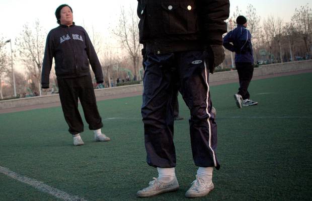 A group of men warm up for a game of football wearing Feiyue brand shoes at a field in Beijing.