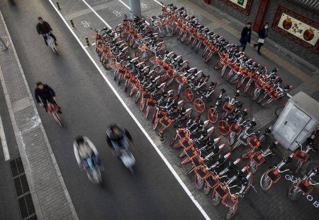 BEIJING, CHINA - APRIL 11: Chinese commuters ride past a large group of Mobike ride share bicycles at a distribution area during rush hour on April 11, 2017 in Beijing, China. The popularity of bike shares has exploded in the past year with more than two dozen providers now battling for market share in major cities across China. The bikes are hailed as an efficient, cheap, and environmentally-friendly solution for commuters, where riders unlock the stationless bicycles using a mobile phone app, drop them anywhere for the next user, and spend as little as 1 yuan ($0.15) per hour. Given the bikes have several users a day - some of them inexperienced riders who swerve into traffic - they are often damaged, vandalized, or abandoned. Companies like Ofo routinely collect the battered two-wheelers and bring them to a makeshift depot that is part repair shop, part graveyard where they are either salvaged or scrapped. The bike shares are powering a cycling revival of sorts in a country once known as the 'Kingdom of Bicycles'. In the early years of Communist China, most Chinese aspired to own a bicycle as a marker of achievement. When the country's economic transformation made cars a more valued status symbol, the bicycle - a Chinese cultural icon - was mocked as a sign of backwardness. The bike share craze is also a boon for manufacturers who are now mass producing over a million bikes a month to meet demand, and the number of shared bike users will reach 50 million in China by the end of the year, according to Beijing-based BigData Research. Not everyone is cheering the revival though, as municipal officials are drafting new regulations to control the chaotic flood of bicycles on streets and sidewalks. (Photo by Kevin Frayer/Getty Images)