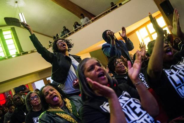 Flint resident Sharon Moore, left, leaps up to shout out her support as she listens to pastor David Bullock during a town hall meeting packed with more than 500 people to discuss the ongoing Flint water crisis on Monday, Feb. 1, 2016 at First Trinity Missionary Baptist Church in Flint, Mich.