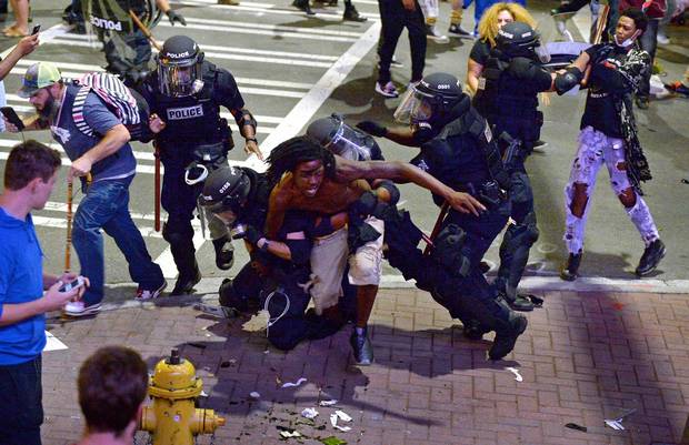 A protester, middle, is taken into custody by Charlotte-Mecklenburg police officers on Wednesday night.