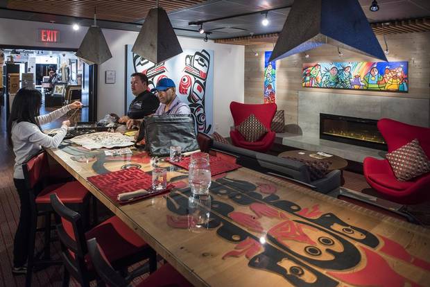 Artists negotiate the sale of their work in the dining area of Skwachays Lodge in Vancouver on April 9, 2015. Yvonne Lai, left, of the Urban Aboriginal gallery, negotiates with artists Grant Pauls and Terrence Cambell over some of their artwork. 