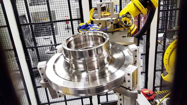 Inside a wire cage, a robot readies material to craft an engine turbine component. It looks like an ornate disc brake you might find in your car—but costs as much as an entire vehicle.