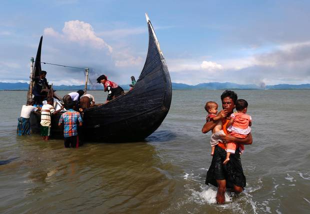 Smoke is seen on Myanmar’s side of border as a Rohingya refugee men carry children from a boat in Shah Porir Dwip, Bangladesh, on Sept. 15, 2017.