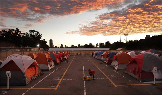 A boy plays as the sun sets over donated tents for homeless families lined up on a parking lot in the city-sanctioned encampment in San Diego in November, 2017. Scores of tents, mobile medical units, portable toilets and showers were brought in to meet the needs of hundreds of homeless people.