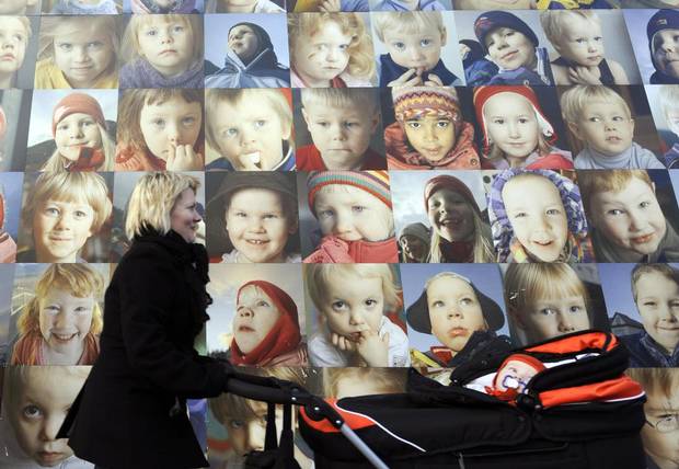 A mother pushes a stroller by a wall with portraits of children on October 8, 2008, in Reykjavik, Iceland.