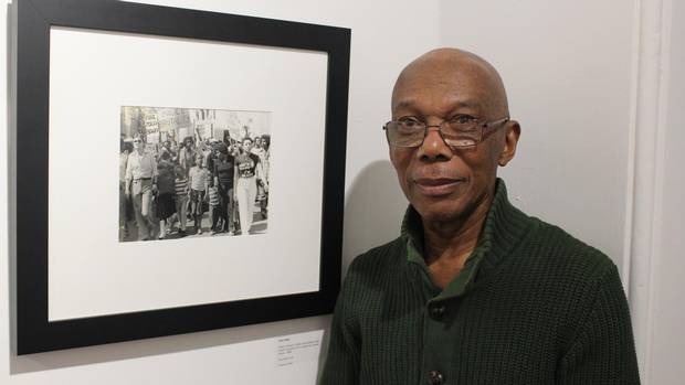 Photojournalist Jules Elder standing next a photograph he took capturing the Albert Johnson protest in 1980.