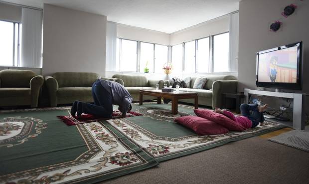 Unable to go to his mosque for prayer service, Ahmad prays in his family’s apartment while daughter Sava, 3, watches TV.