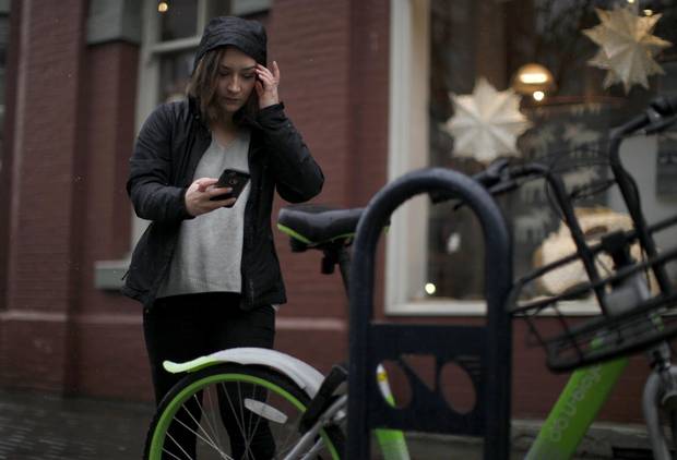 Carly Eldstrom uses the U-Bicycle app on her phone to scan a barcode to unlock a bicycle along Douglas St. in Victoria, B.C.