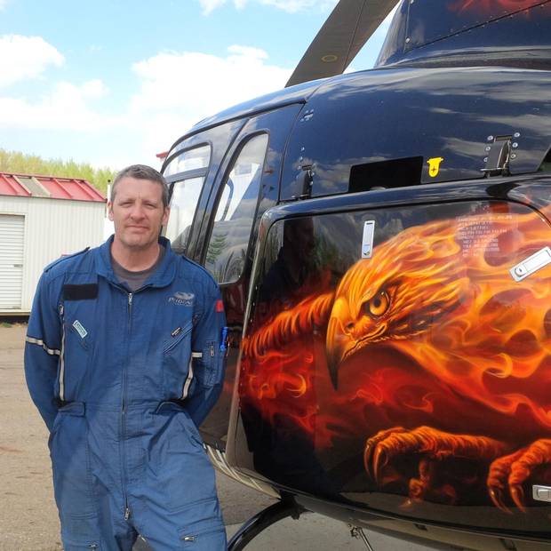 Ken Saumure, a pilot with Phoenix Heli-Flight stands beside a helicopter after dousing a hotspot near the facility in Fort McMurray.