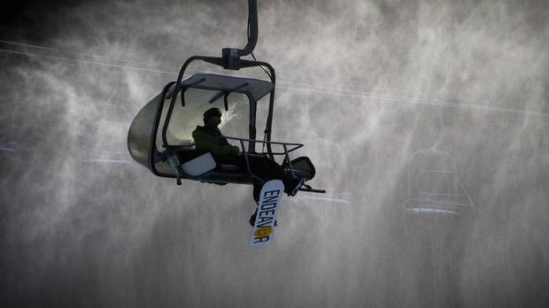 A snowboarder rides the Wizard Express chairlift down Blackcomb Mountain as snow from a snowgun hangs in the air in Whistler, B.C.