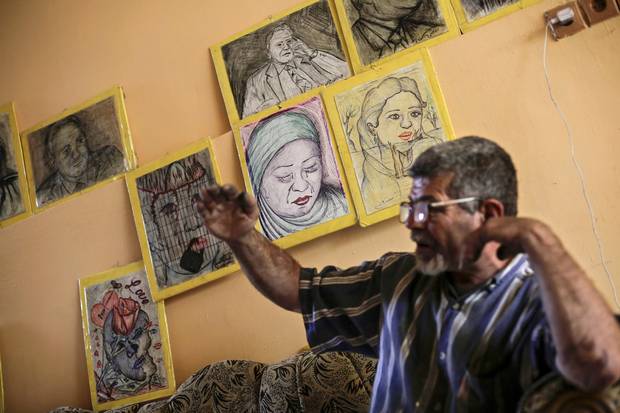 Iraqi painter Mustafa al-Taee sits in front of a display of his art work. He expected to be shot by Islamic State militants