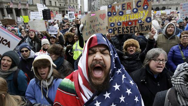 Izzy Berdan, of Boston, center, wears an American flags as he chants slogans with other demonstrators during a rally on Sunday, Jan. 29, 2017, in Boston.