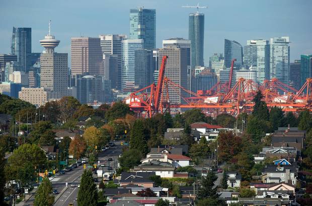 The downtown skyline and cranes at Port Metro Vancouver are seen in the distance behind houses in east Vancouver, B.C., on Sept. 23, 2015. Vancouver is becoming a city where many of its residents are shuffling in together and squeezing in at a steady pace.