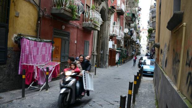 People ride a scooter through a Naples alleyway.