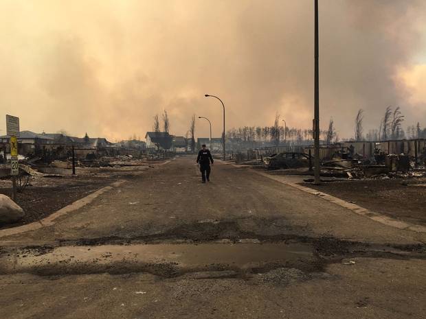 In this image released by the Alberta RCMP on May 5, 2016, a police officer walks on a road past burned down houses in Fort McMurray, Alberta. 