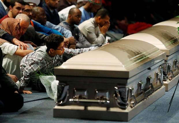 A mourner places his hand on one of the caskets during funeral services for three of the victims, Feb. 3, 2017.