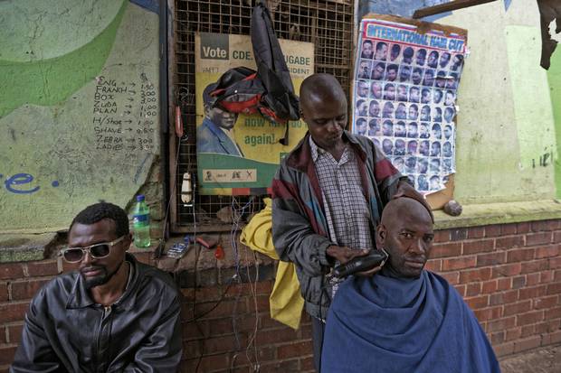 Nov. 16: A man has a shave at a street barber, next to a covered poster of Mr. Mugabe, in the low-income neighbourhood of Mbare in Harare.