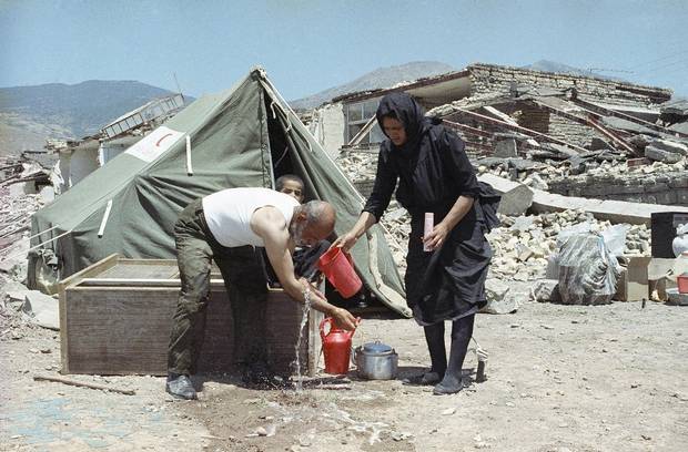 An Iranian man gets help from his wife as he cleans up outside their tent in Manjil, Iran, on June 28, 1990. They lost their home in the earthquake.