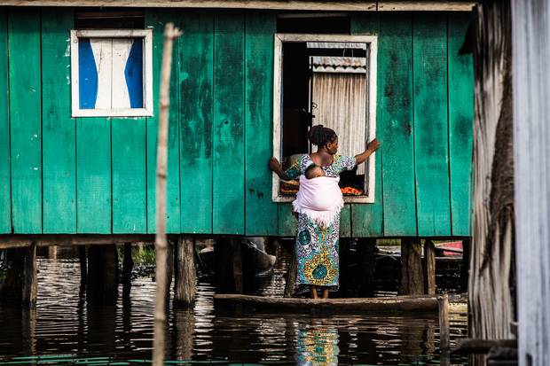 A woman stands on her boat outside of a house in So-Ava. For many in the community, small canoes are their only link to the outside world.