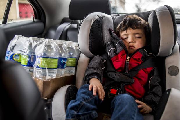 Liam Briones sleeps in a car seat as his father drives around from fire station to fire station gathering water for the week.