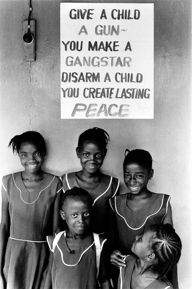 Children in school uniform pose in front of a poster promoting peace and disarmament. Sierra Leone, 1999.