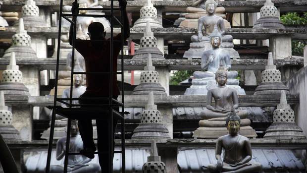 A silhouetted worker climbs a ladder near rows of buddha statues at the Gangaramaya Temple complex in Colombo, Sri Lanka, on Wednesday, July 22, 2015.