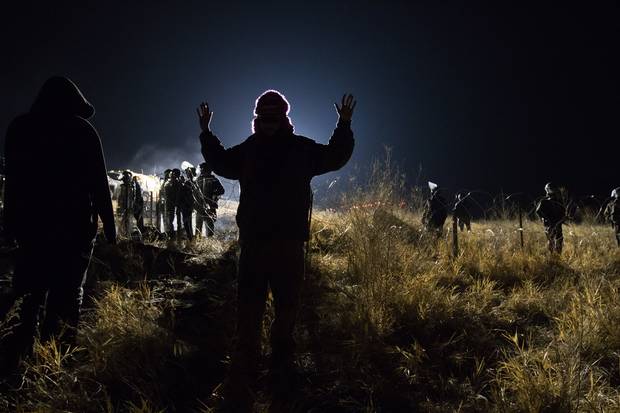 A demonstrator, or “water protector,” meets a police blockade on Highway 1806 near Cannon Ball. Many people were injured when, in sub-zero temperatures, police deployed water cannons, pepper spray, tear gas, rubber bullets and percussion grenades.