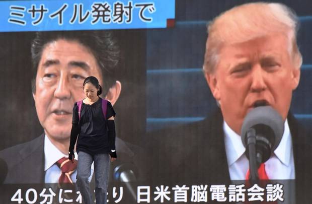 A woman walks in front of a huge screen displaying Japanese Prime Minister Shinzo Abe (L) and US President Donald Trump (R) in Tokyo on August 29, 2017.
