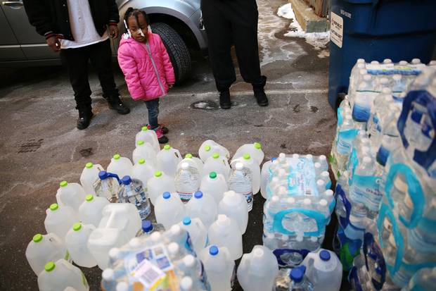 Jazmine Davis stands next to water cases and jugs of water that will be loaded onto a U-Haul truck for the people of Flint in Kalamazoo, Mich.