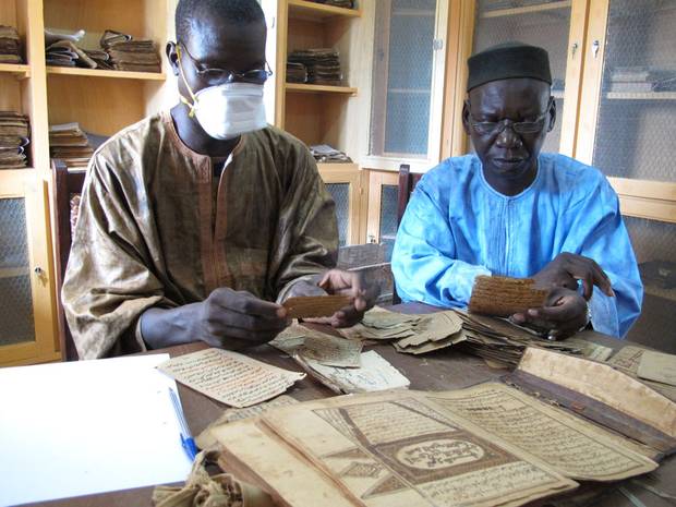 Archivists Aboubakar Yaro and Alphamoye Djeite study ancient manuscripts in a library in the Malian town of Djenne. (Yaro is wearing a mask to protect him from dust.) They are cataloguing the manuscripts as part of a British Library project to digitize copies of 200,000 manuscript pages in Djenne.