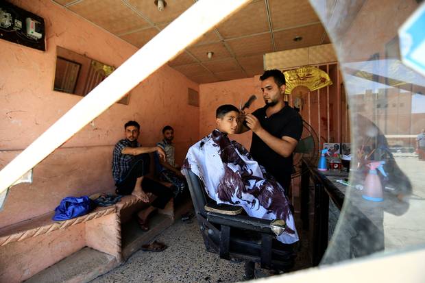 A barber shaves the head of a boy at his shop in West Mosul, Iraq July 20, 2017.