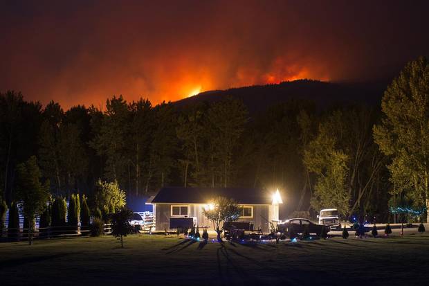 A wildfire burns on a mountain behind a home in Cache Creek, B.C., in the early morning hours of July 8.