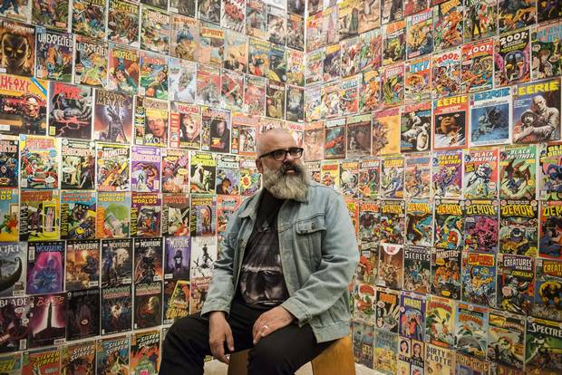 Exhibition curator Jim Shedden poses against a wall displaying hundreds of influential comic books.