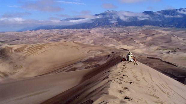 A hiker summits a dune and views the panorama of the Great Sand Dunes National Preserve in Colorado.