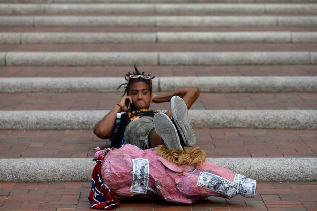 A protester in Cleveland reclines on a set of stairs using a Donald Trump pig puppet as a footrest.