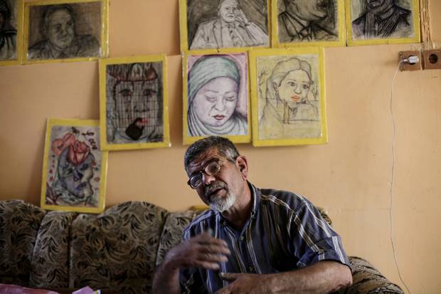 Iraqi painter Mustafa al-Taee sits in front of a display of his art work at his home in the northern town of Hamam al-Alil, near Mosul, Iraq