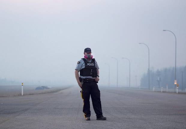 An RCMP officer wears a gas mask to combat the smoke as he mans a checkpoint on the highway to Fort McMurray, Alberta on Friday, May 6, 2016.