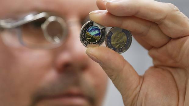 The freshly painted two dollar glow in the dark coin is inspected by production operator Rene Tetrault at the Royal Canadian Mint in Winnipeg Tuesday, April 4, 2017.