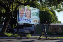 FILE - Luis Servin, an unemployed municipality worker who now sells banana and lemons, walks past a billboard promoting presidential candidate Efrain Alegre and running mate Soledad Nunez, in Asuncion, Paraguay, April 21, 2023. The country's general elections are scheduled for April 30th. Analysts expect a tight race with the opposition fueled by anger over high levels of corruption and the deficiencies in the health and education systems that worsened during the COVID-19 pandemic. (AP Photo/Jorge Saenz, File)