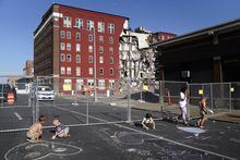 Children draw on the ground with chalk at the scene where an apartment building partially collapsed on Sunday afternoon, Tuesday, May 30, 2023, in Davenport, Iowa. Five residents of the six-story apartment building remained unaccounted for and authorities feared at least two of them might be stuck inside rubble that was too dangerous to search. (AP Photo/Erin Hooley)