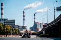(FILES) This file photo taken on March 6, 2017 shows a man riding his scooter near the Shanghai Waigaoqiao Power Generator Company coal power plant in Shanghai. - China must stop building new coal power plants and ramp up its wind and solar capacity if it wants to become carbon neutral by 2060, researchers said on November 20, 2020. (Photo by JOHANNES EISELE / AFP) (Photo by JOHANNES EISELE/AFP via Getty Images)